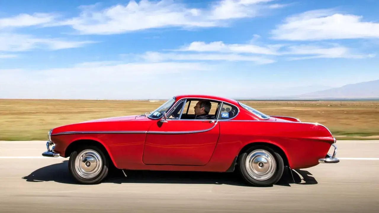 Irv Gordon kör sin röda Volvo P1800 över ett öppet fält under en klarblå himmel.