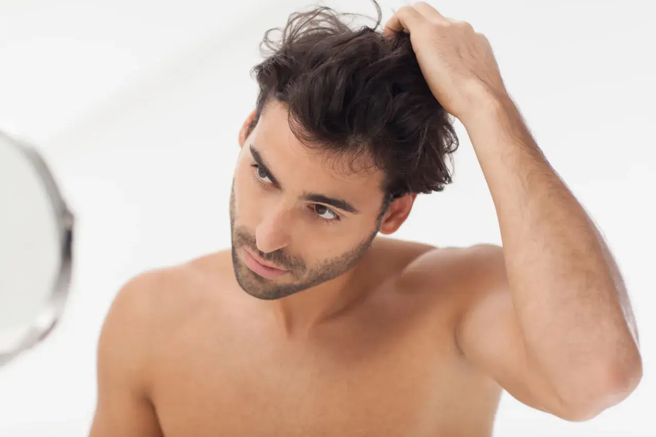 Hombre revisando su cabello en el espejo, parte de su rutina de cuidado del cabello hombre.