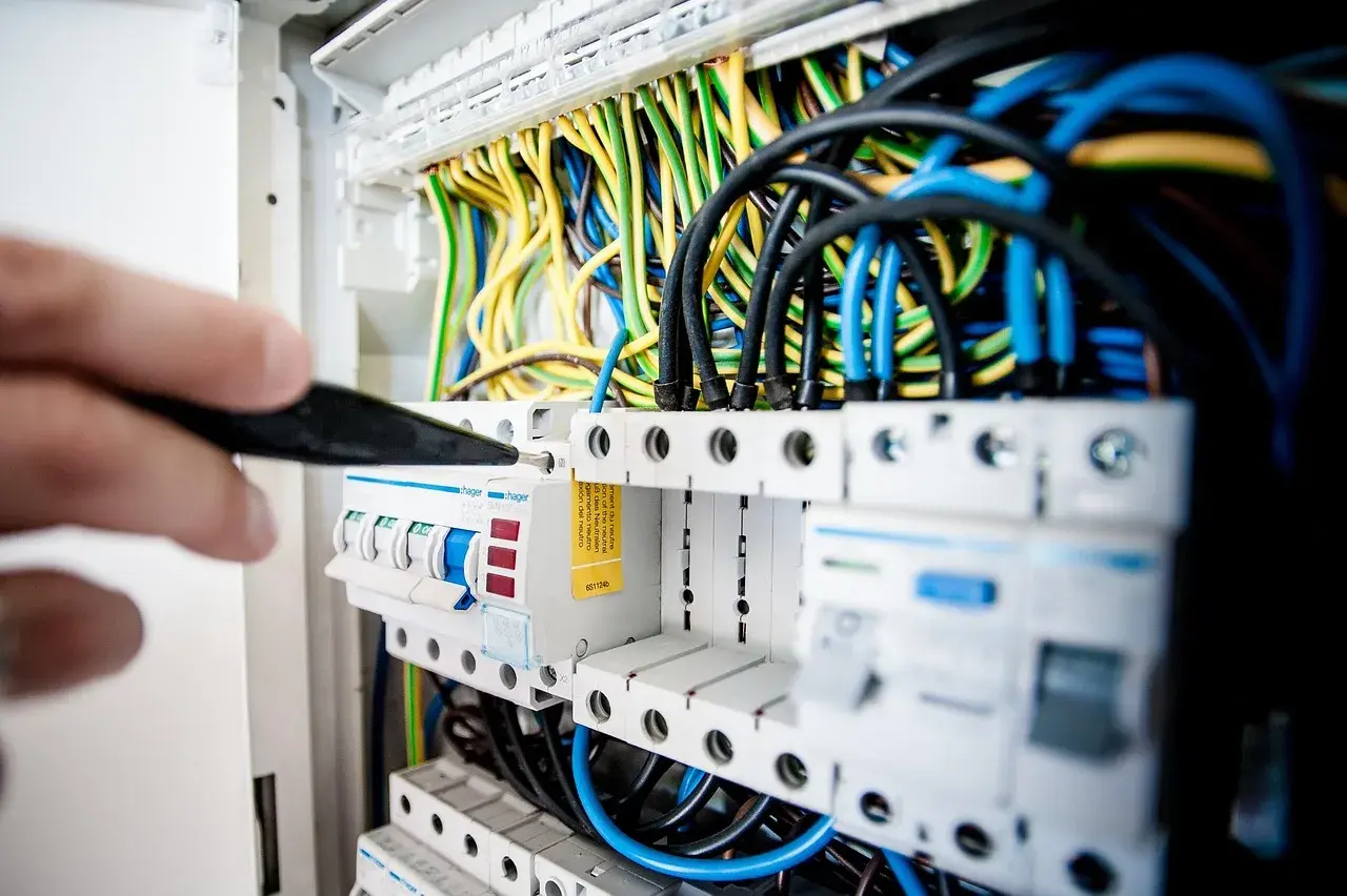 Ręka majstruje przy bezpiecznikach, tworząc instalację elektryczną w domu. Kolorowe przewody tworzą plątaninę.