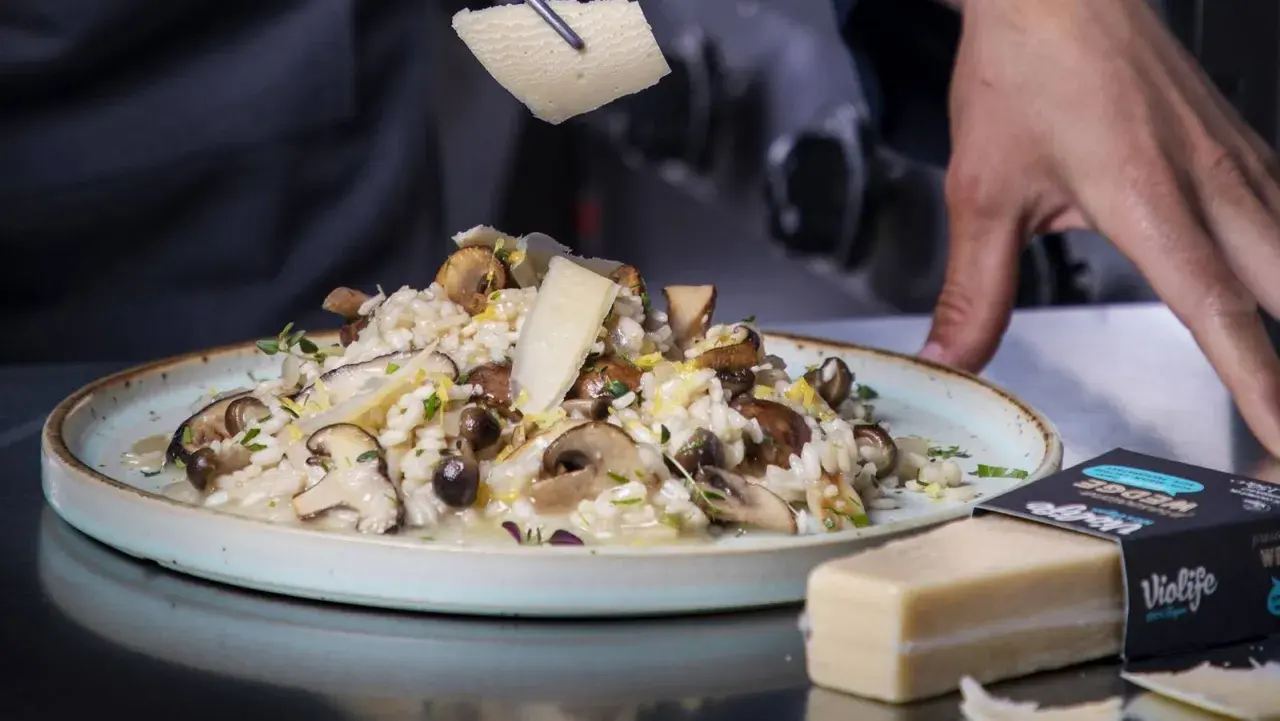 Krämig risotto svamp toppas med hyvlad ost. En vegansk ostbit ligger bredvid.