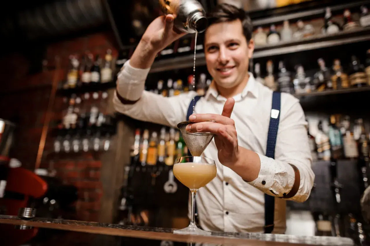 Uśmiechnięty barman przelewa drinka przez sitko. Czy barman może pić w pracy? Ten z pewnością tworzy pyszne koktajle!