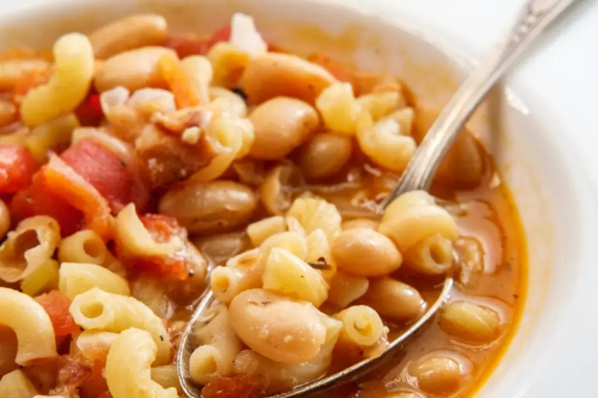 Un cucchiaio raccoglie un saporito piatto di pasta e fagioli, con maccheroni, fagioli bianchi e pomodoro in un brodo ricco.