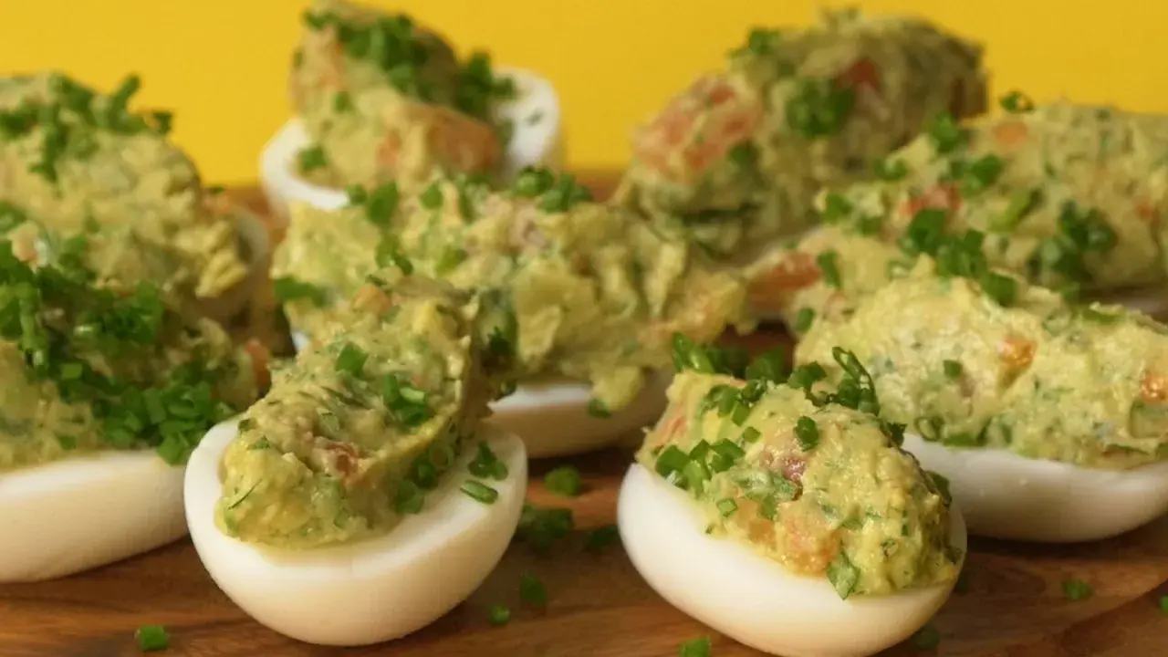 Jajka faszerowane guacamole, udekorowane szczypiorkiem, wyglądają apetycznie na drewnianej desce.