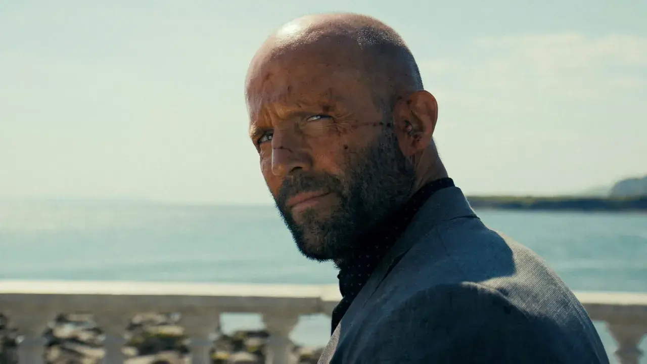 En skadad man med skägg och rakad skalle, klädd i kavaj, blickar ut över havet. En scen från biodlaren film.