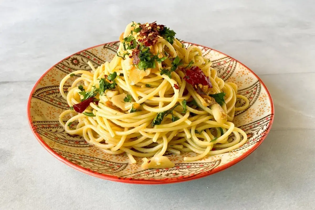 Un plato de spaghetti aglio e olio, con ajo laminado, perejil fresco y hojuelas de chile rojo, servido en un plato decorado.