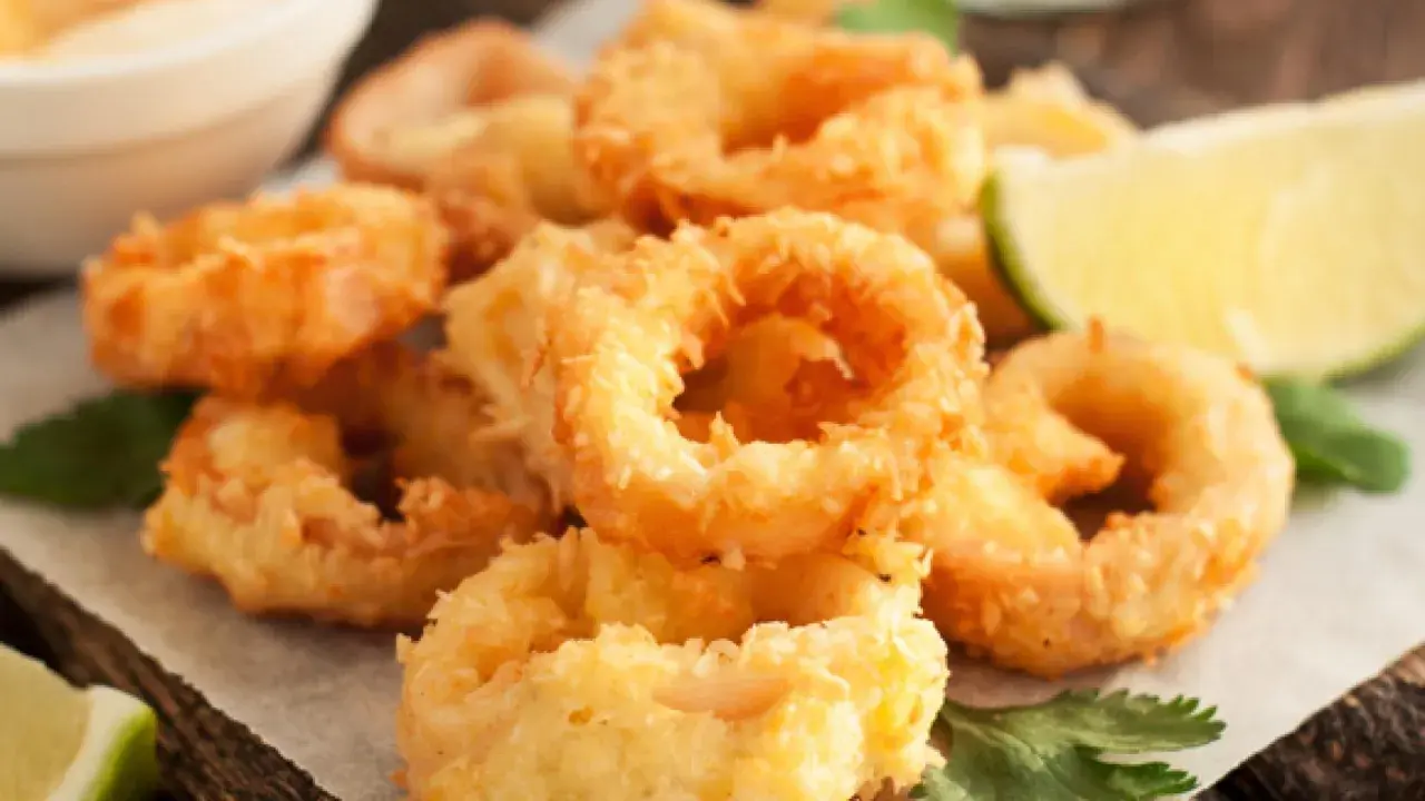 Crujientes calamars a la romana, dorados y listos para disfrutar, acompañados de gajos de limón y perejil fresco.