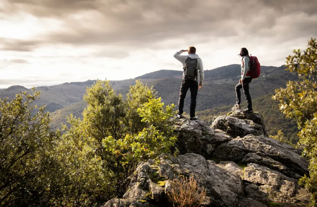 Deux randonneurs contemplent un paysage montagneux depuis un promontoire rocheux, profitant d'une vue panoramique.