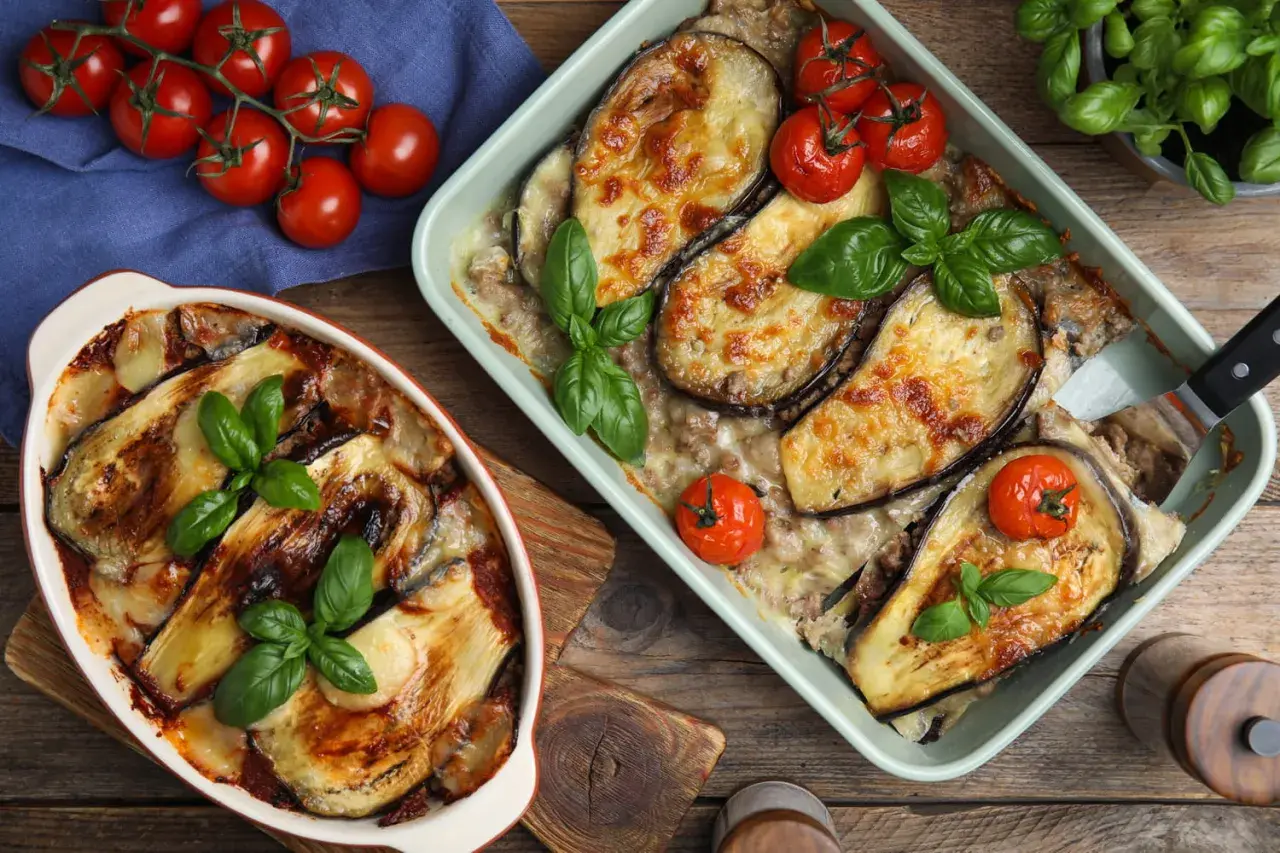 Deux plats d'aubergine à la parmesane au four, dorés et gratinés, garnis de tomates cerises et de basilic frais.