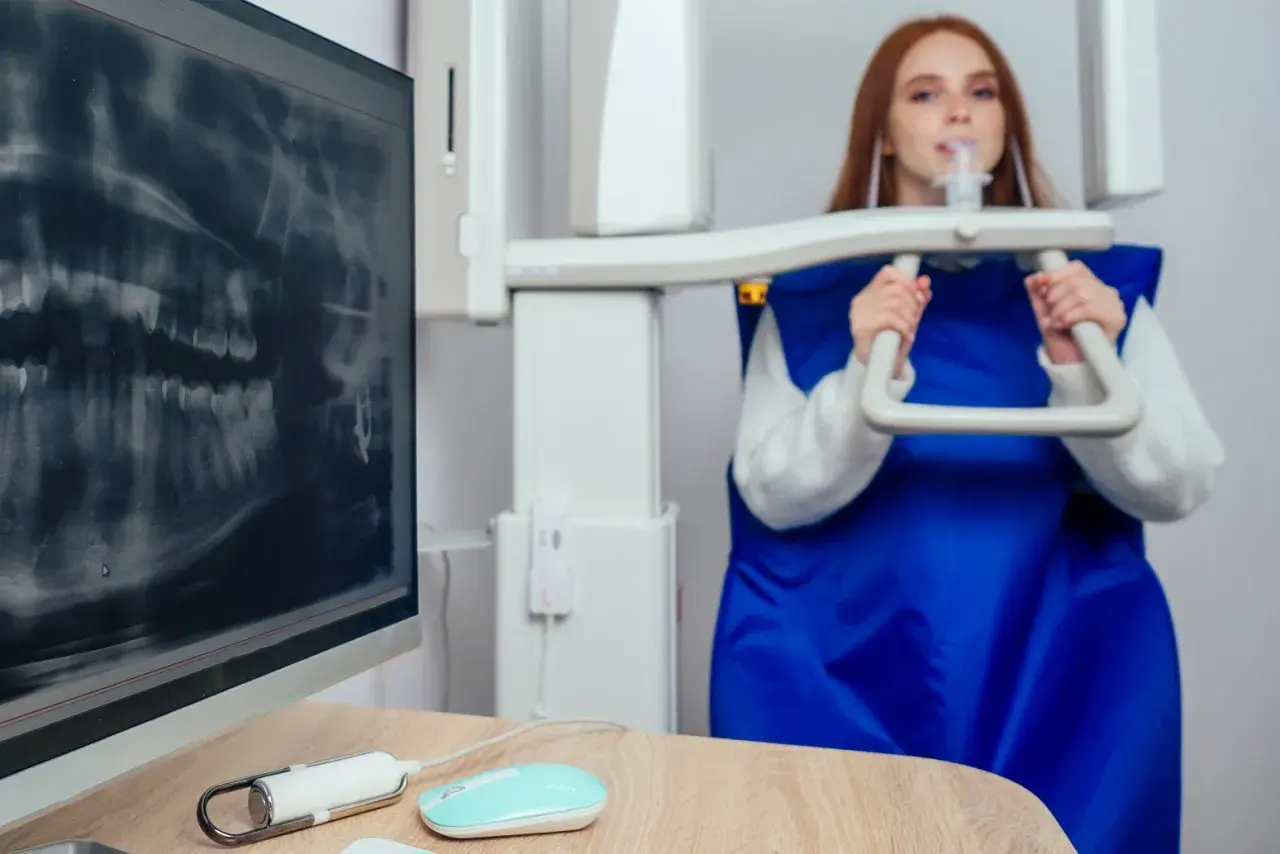 RTG zębów podczas ciąży jest bezpieczne. Kobieta w fartuchu ochronnym podchodzi do aparatu RTG.