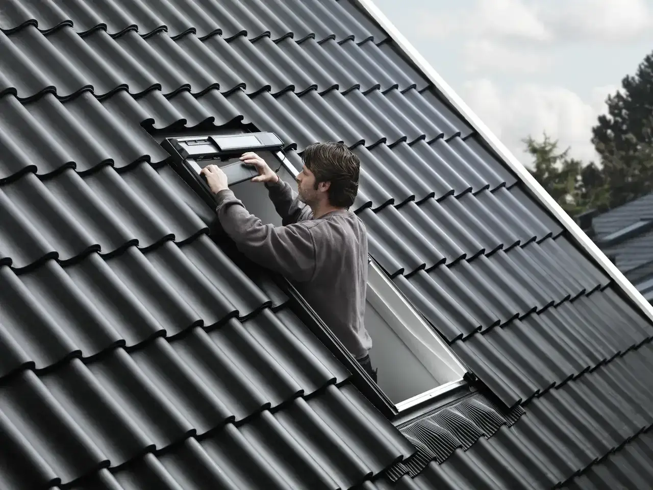 Uomo sul tetto che installa una finestra, la casa prende luce dal tetto.