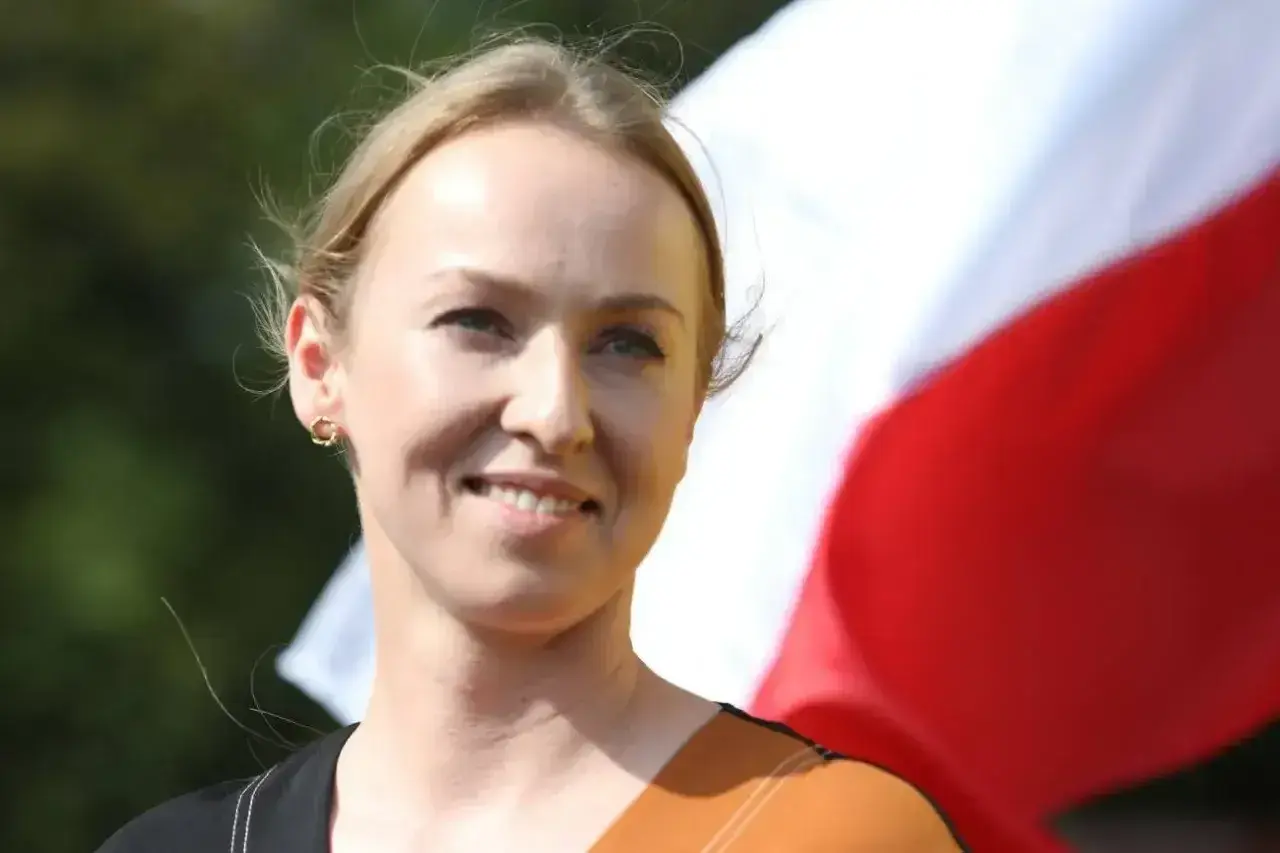 Uśmiechnięta Urszula Brzezińska-Hołownia, której wiek nie jest widoczny, na tle polskiej flagi.