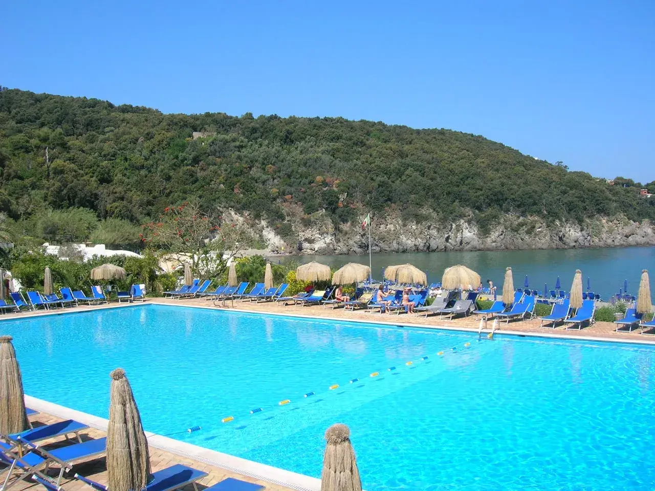Piscina con lettini e ombrelloni, vista mare e collina verde. Informazioni su Negombo prezzi e orari per una vacanza rilassante.