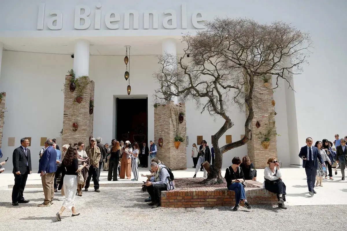 Ludzie spacerują przed budynkiem z napisem "la Biennale". Atmosfera jak na Biennale Wenecja 2026.