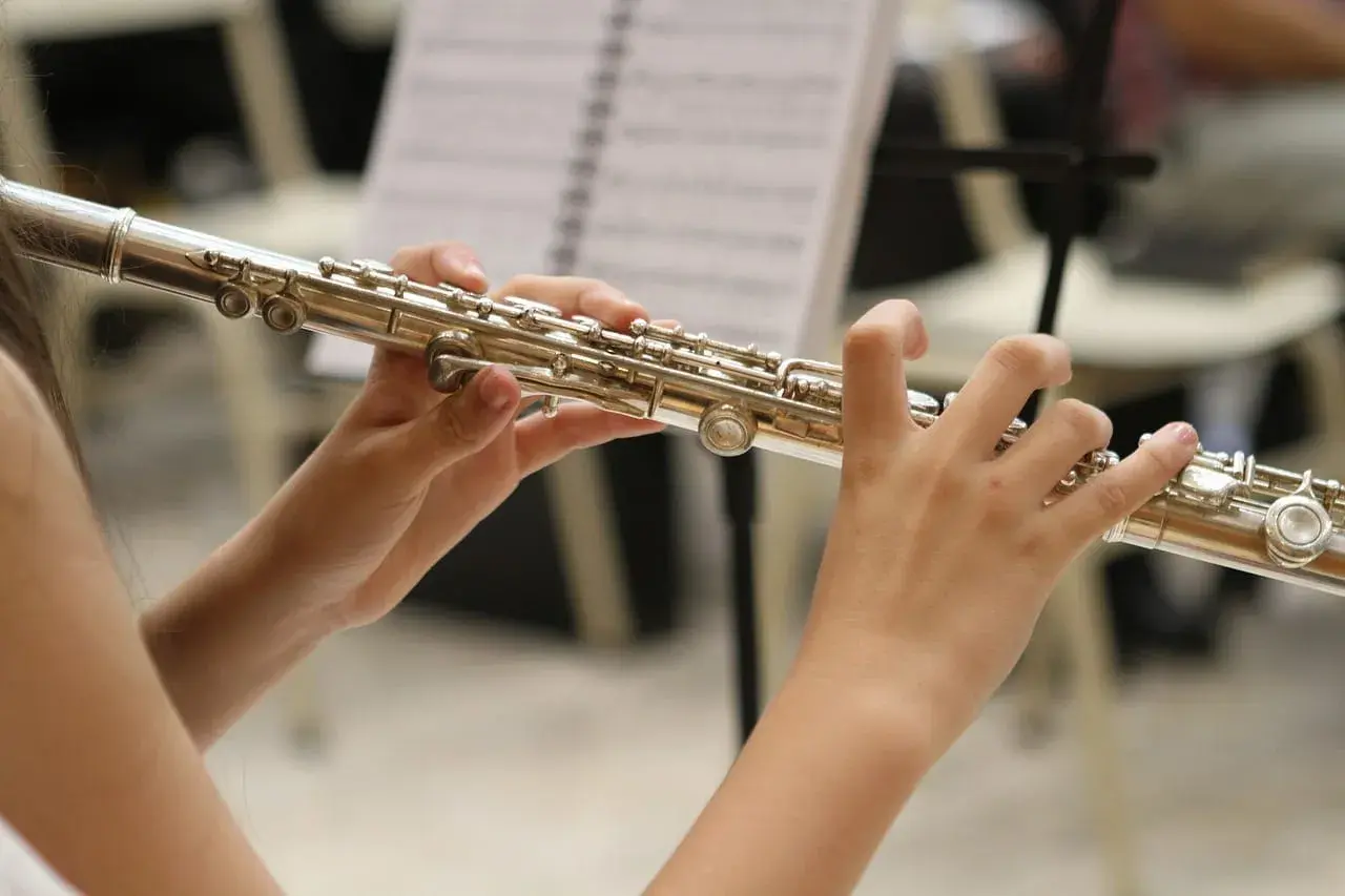 Dłonie grają na instrumencie podobnym do fletu, z nutami w tle.