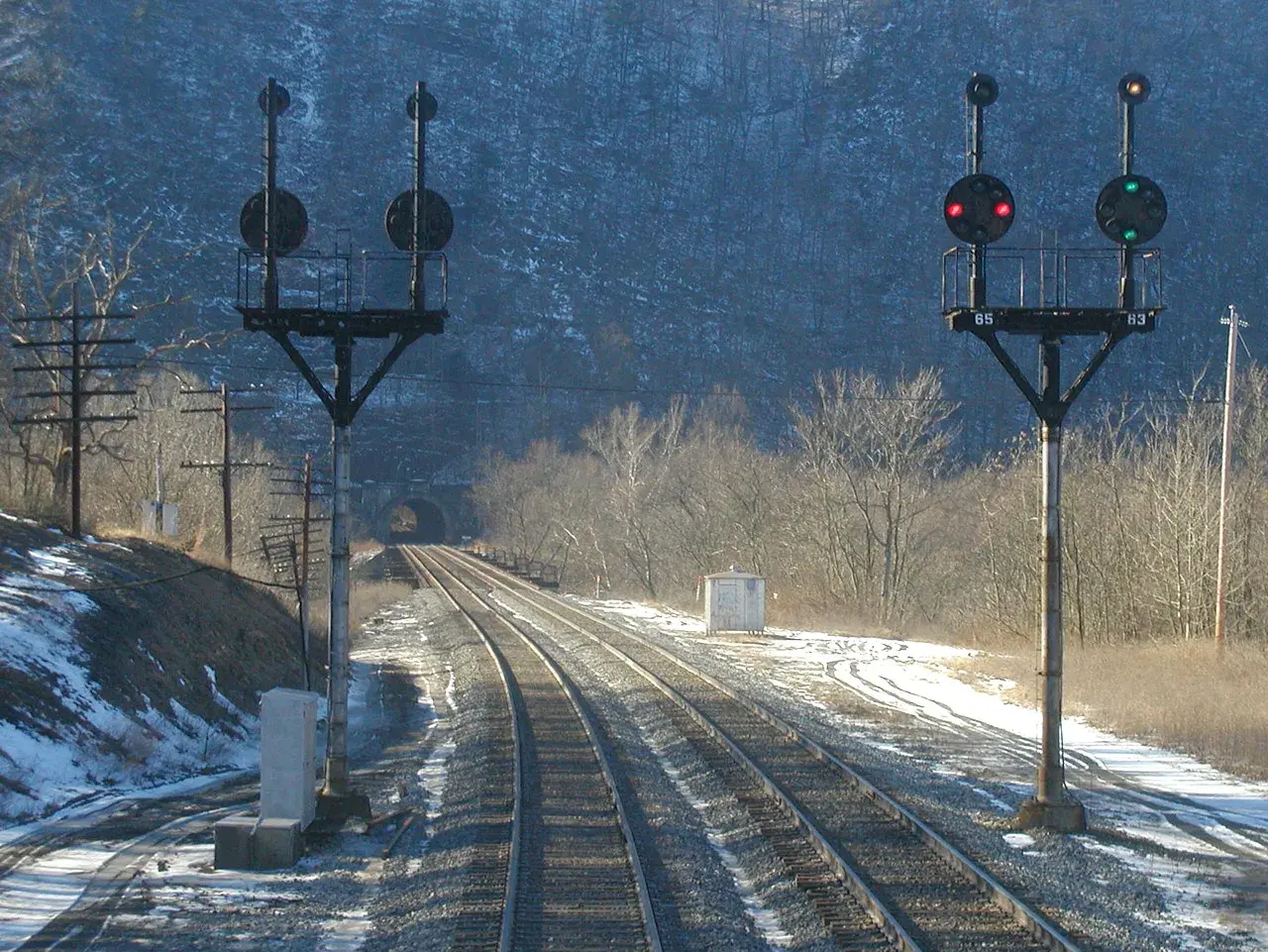 Dwa semafory kolejowe z czerwonymi i zielonymi światłami na tle tunelu i zaśnieżonego krajobrazu.