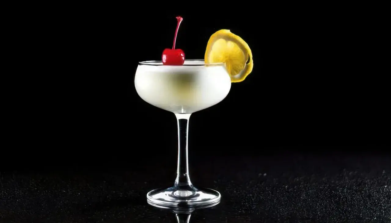 En elegant drink, en "white lady", med körsbär och citronskiva på svart bakgrund.