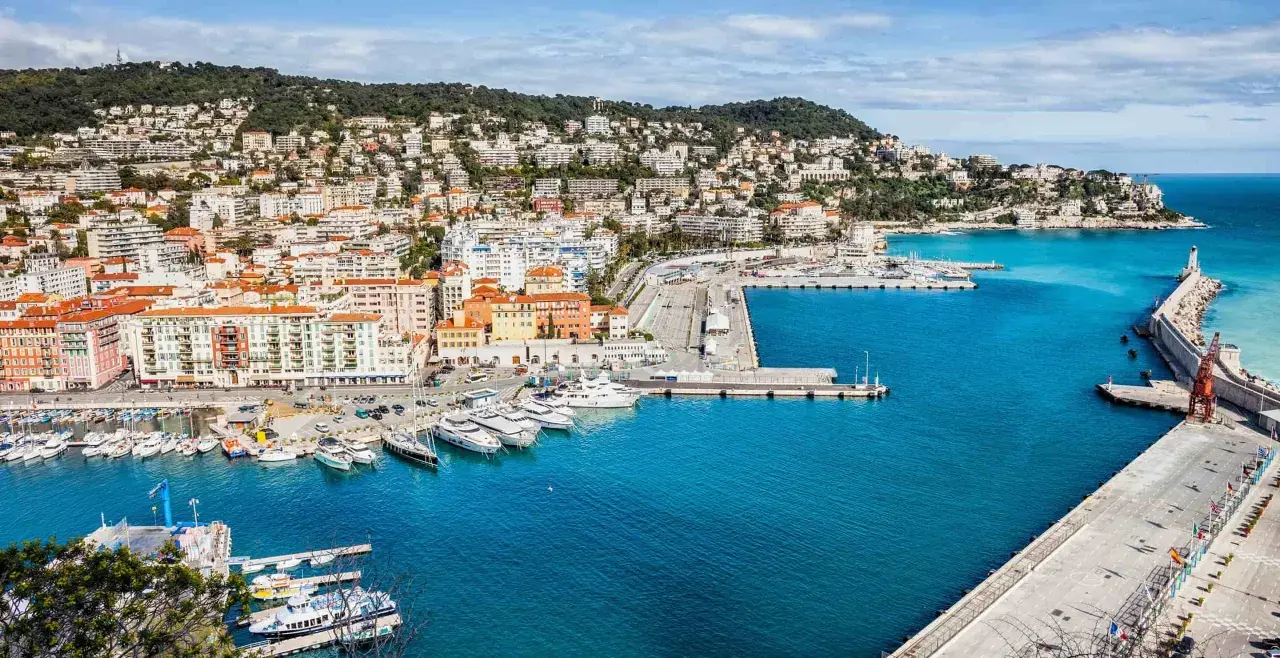 Vue panoramique du port de Nice, avec des yachts amarrés et des bâtiments colorés. On imagine un repas chez Juliette, menu ensoleillé.
