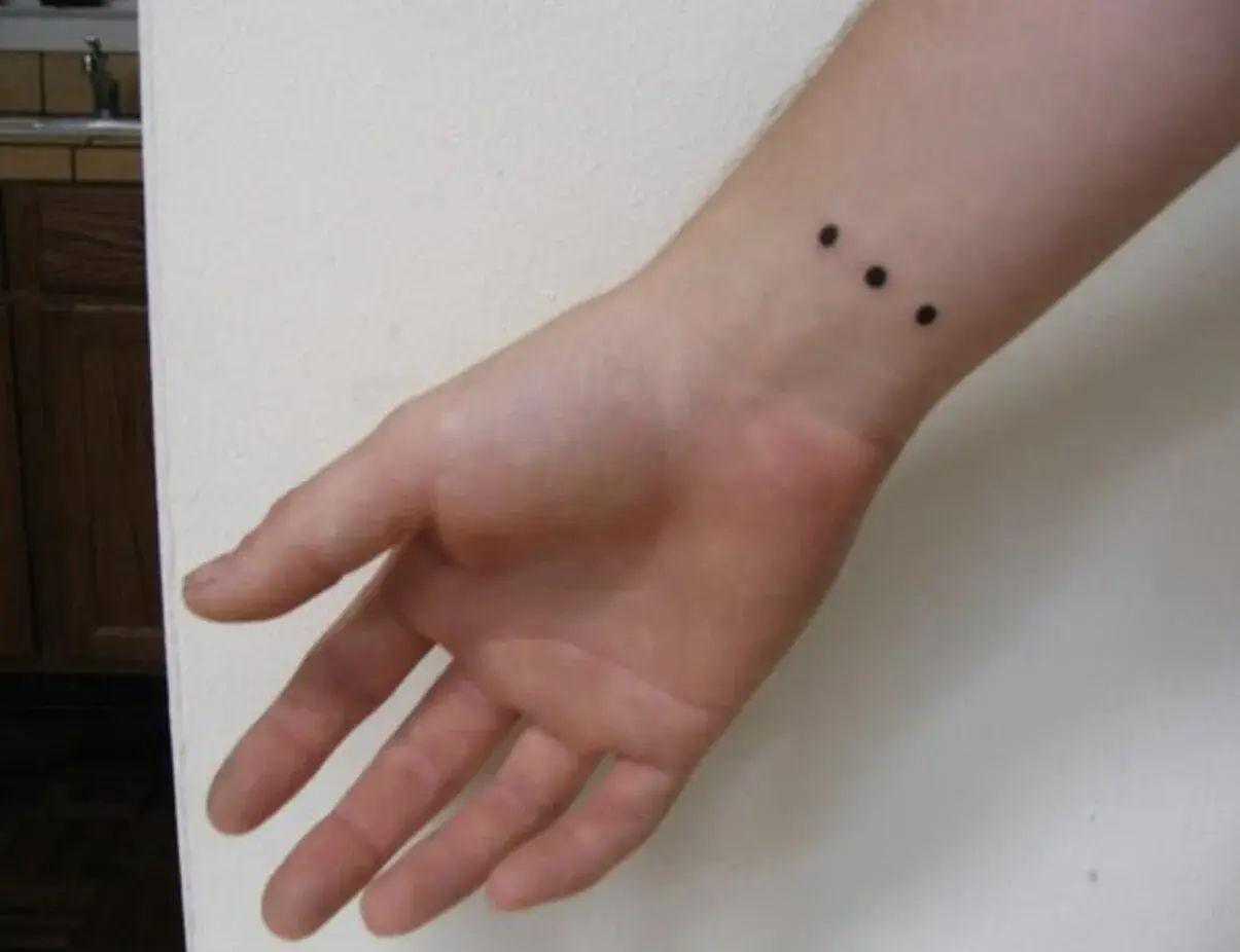 Muñeca con un discreto tatuaje de tres puntos negros alineados.
