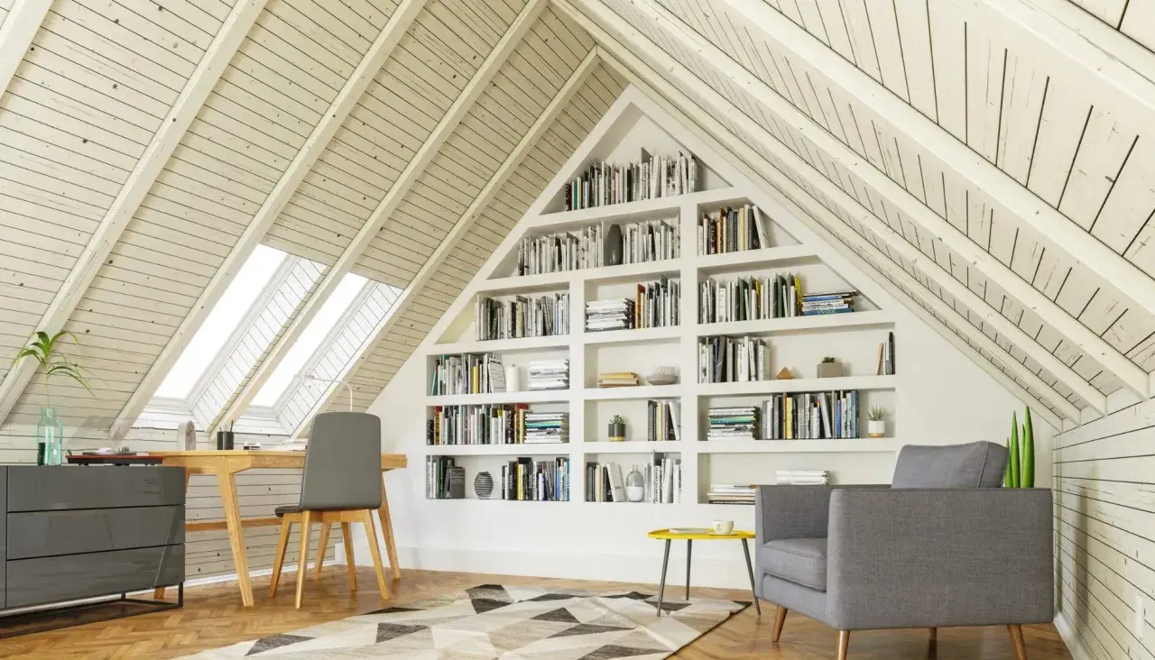 Gemütlicher Arbeitsplatz mit Bücherregalen im Dachausbau. Ein Schreibtisch unter Dachfenstern und eine Leseecke laden zum Verweilen ein.