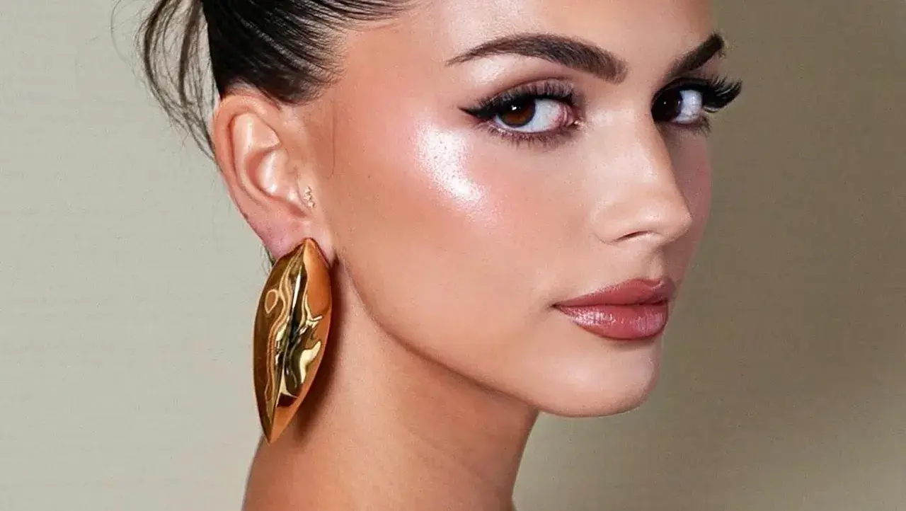Rostro con maquillaje radiante, destacando el uso de iluminador en barra para un brillo natural.