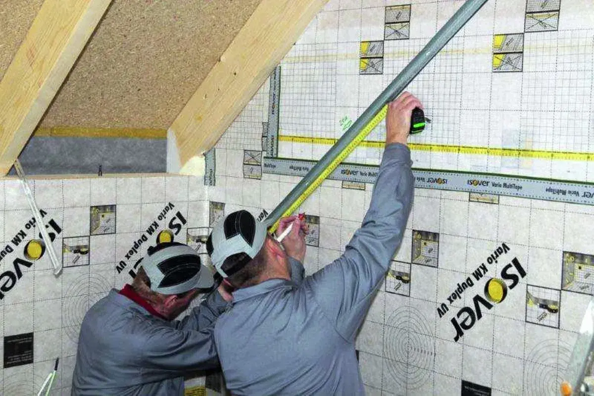 Pracownicy mierzą i zaznaczają punkty na konstrukcji profili na skosach poddasza, przygotowując je do dalszych prac.