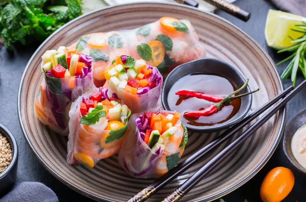 Kolorowe spring rolls z krewetkami, warzywami i miętą, podane z sosem chili i limonką. Pyszna przekąska.