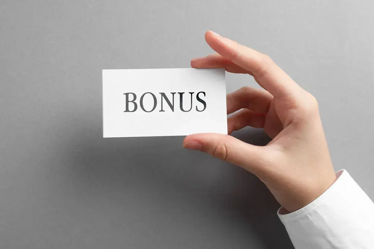 Dłoń trzyma kartkę z napisem "BONUS". To może być dodatek stażowy, który czeka na Ciebie!