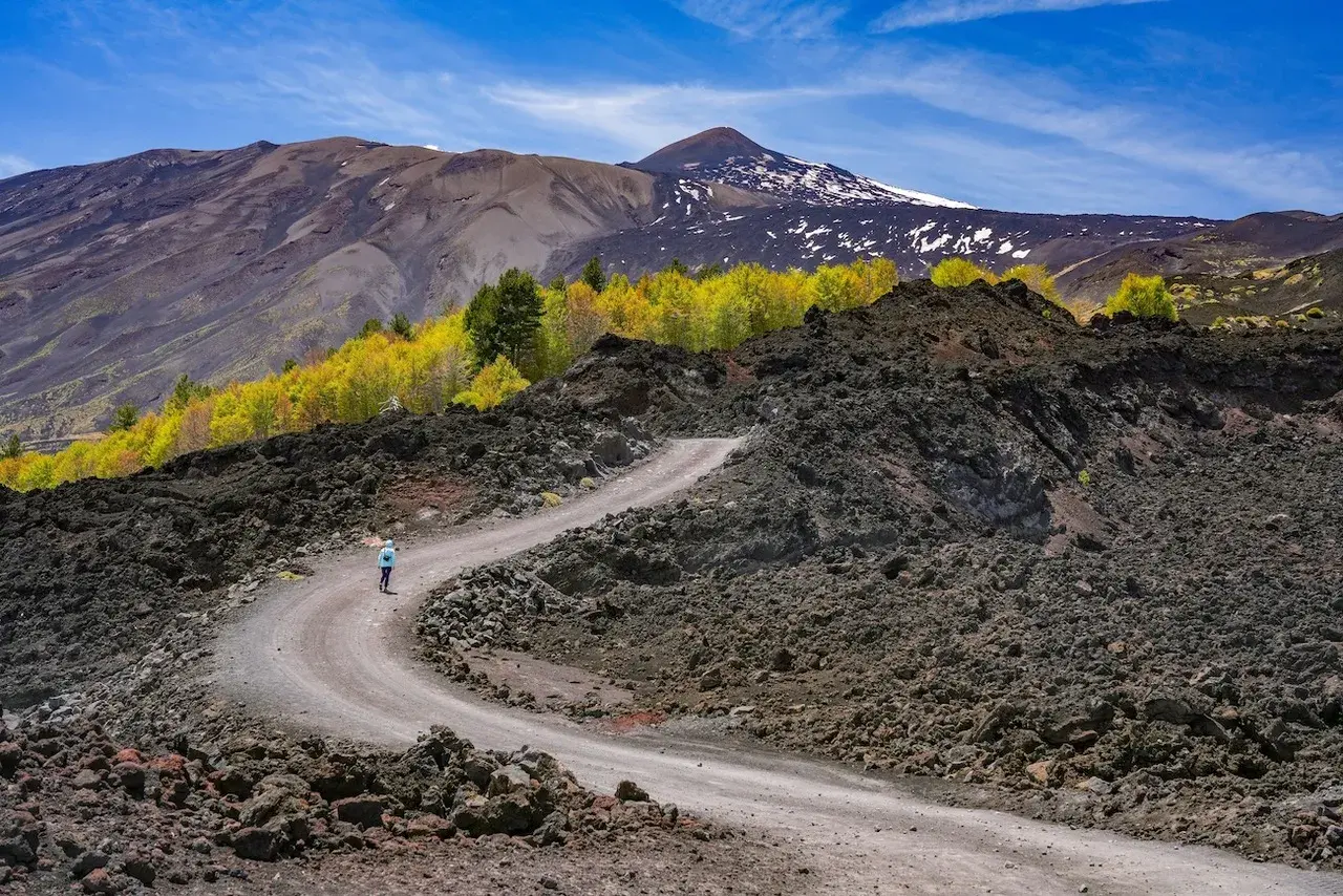 Sentiero tortuoso su Etna, ideale per una **randonnée Etna sans guide**. Paesaggio lunare con rocce laviche e vegetazione autunnale.