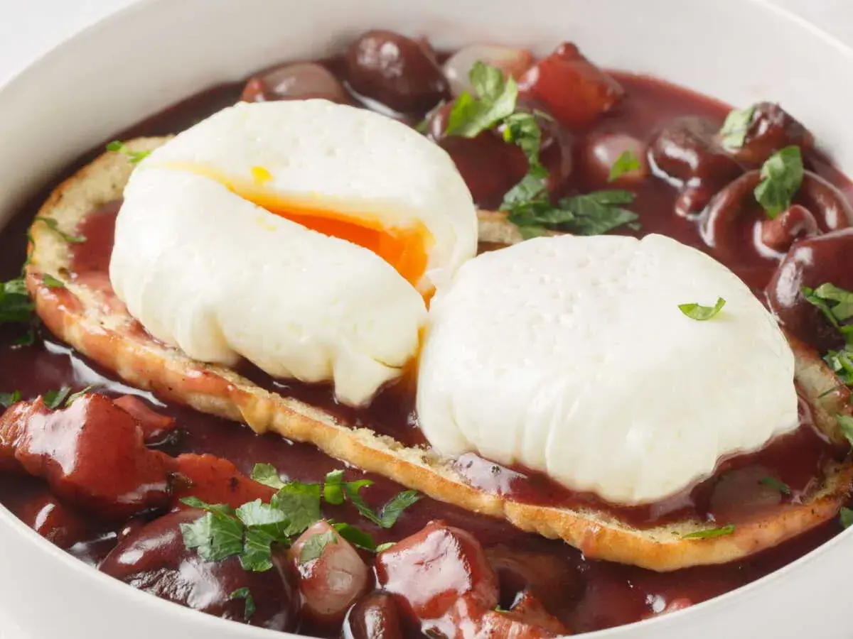 Un œuf meurette, deux œufs pochés sur toast, baignant dans une sauce au vin rouge avec lardons et oignons.