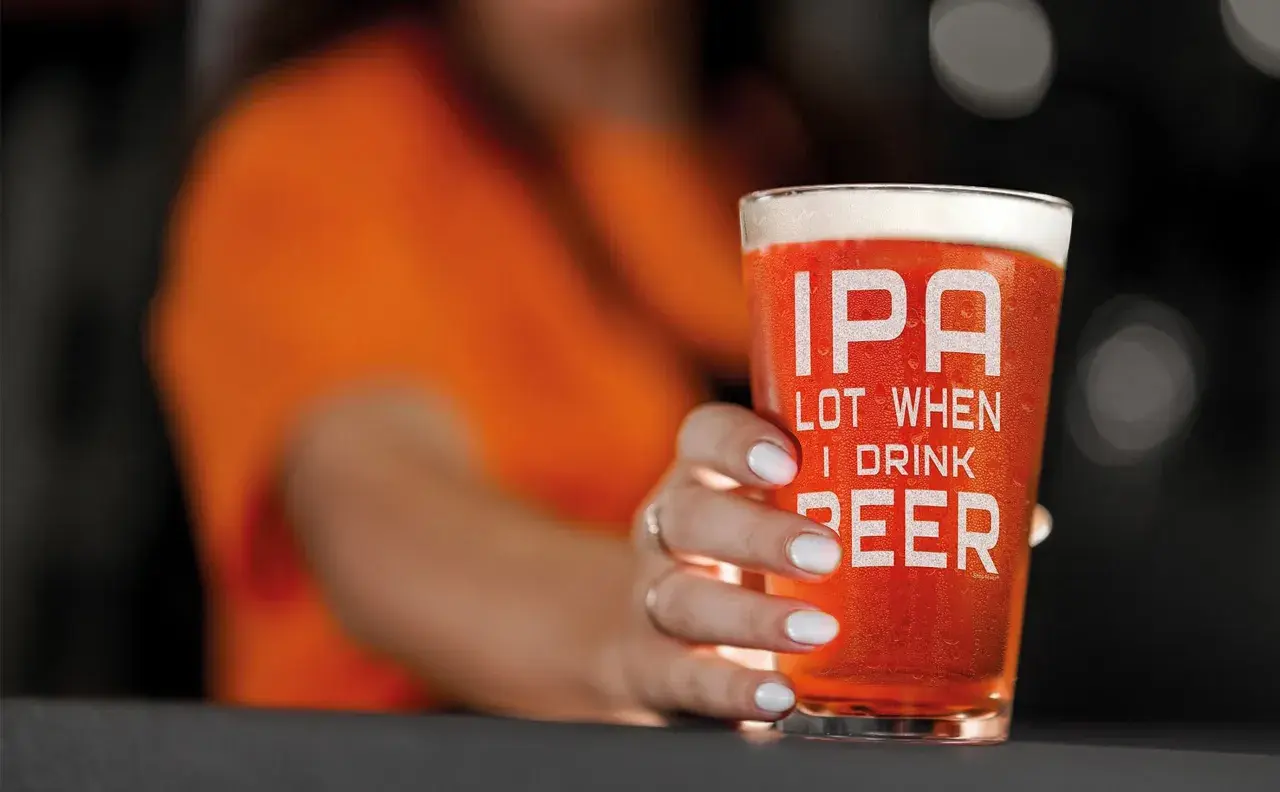 Un bicchiere di IPA con la scritta "IPA LOT WHEN I DRINK BEER" tenuto da una mano con unghie bianche.