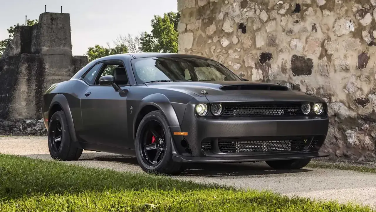 Mroczny Dodge Challenger Demon, z potężną maską i agresywnym grillem, stoi przed kamienną ścianą.