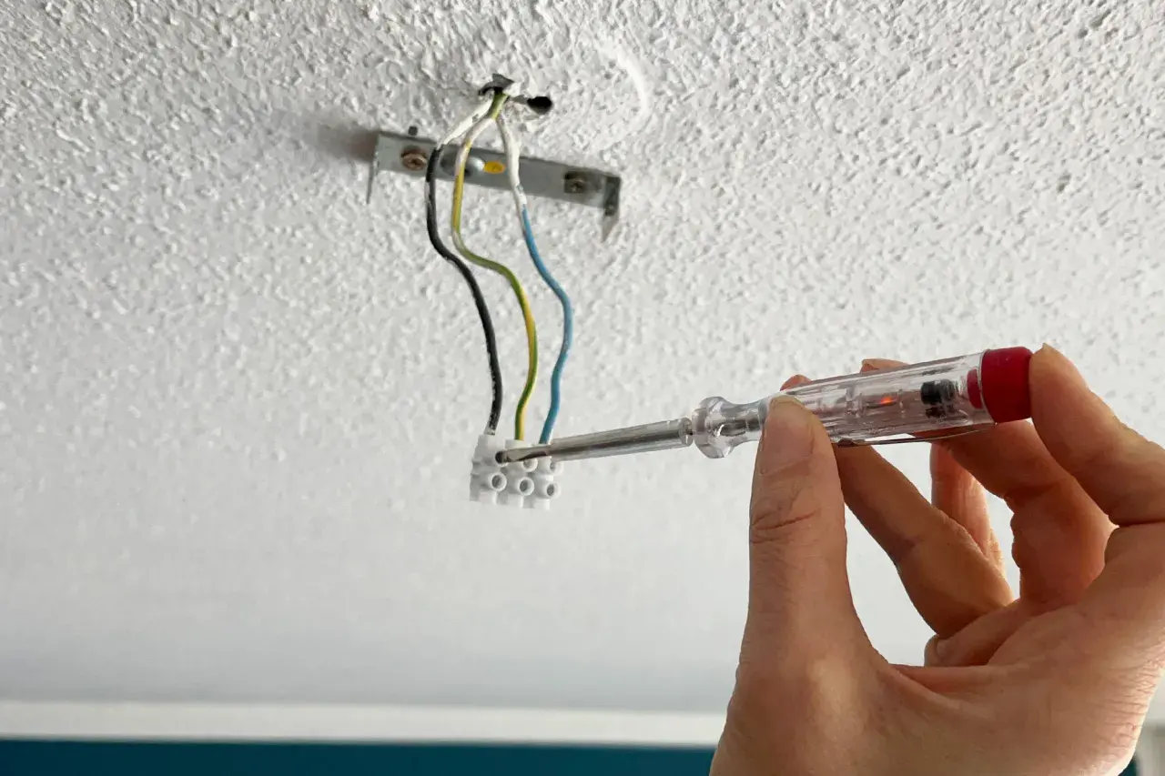 Hand mit Schraubendreher prüft Kabel für die Montage einer Lampe an der Decke.