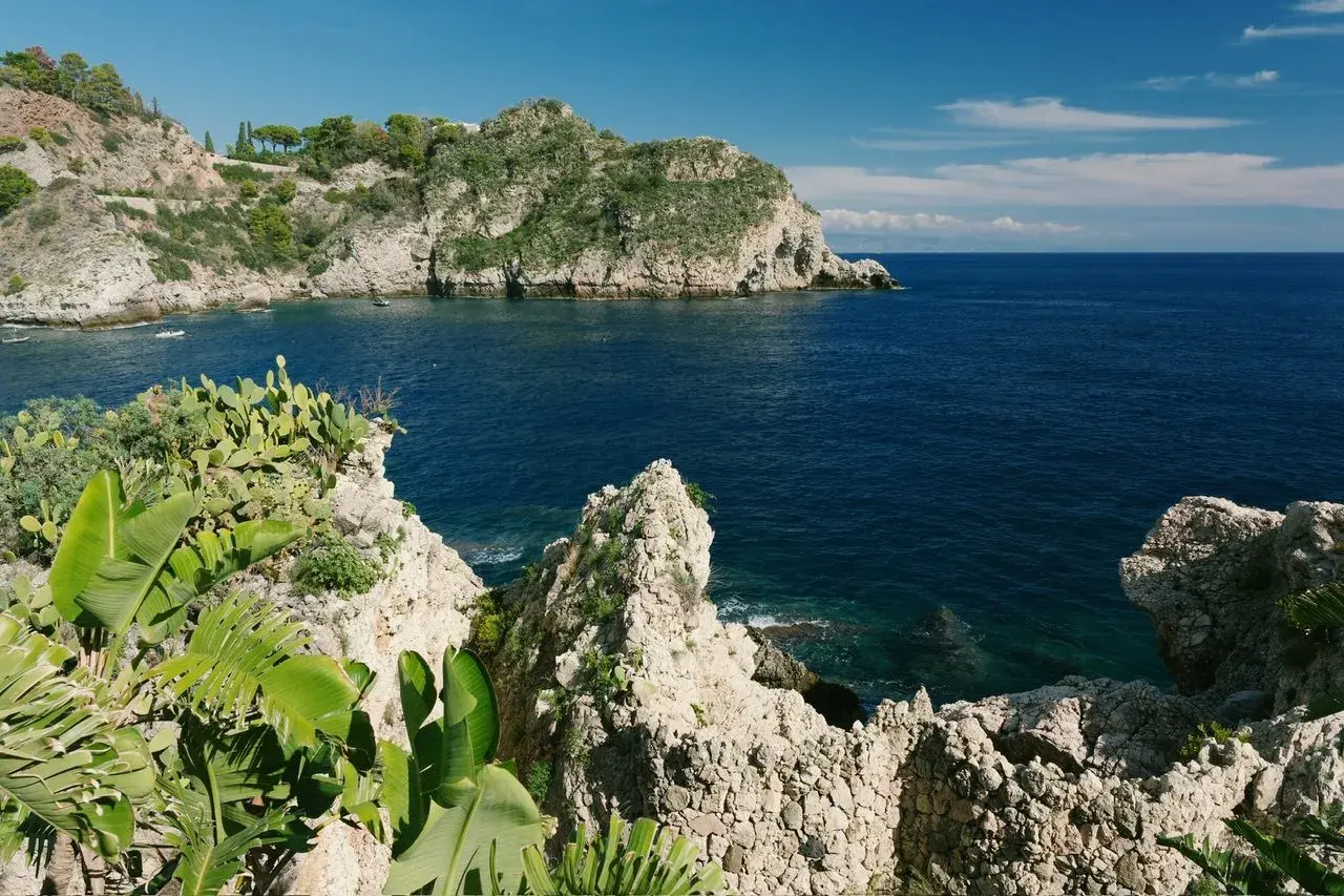 Scogliera verdeggiante e mare blu intenso al lido Isola Bella Taormina.