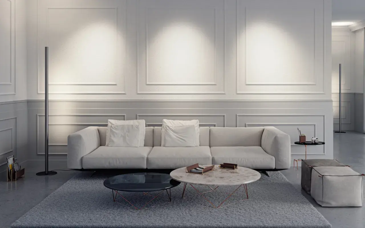 Elegante salón con sofá blanco, mesas de centro y una lámpara de pie sin pantalla que ilumina la pared con molduras.