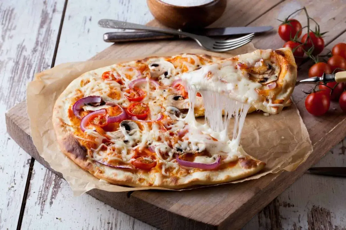 Eine köstliche Pizza mit geschmolzenem Käse, Tomaten, Zwiebeln und Pilzen. Der Teig, wie vom echten Italiener, wurde im Thermomix zubereitet.