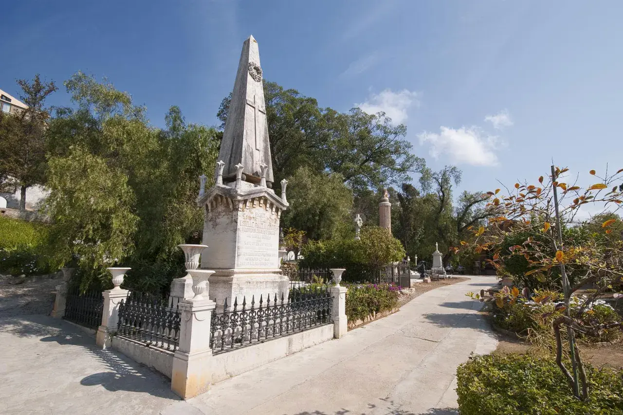 Un obelisco y monumentos se alzan en el cementerio de los ingleses, un lugar sereno bajo un cielo azul.