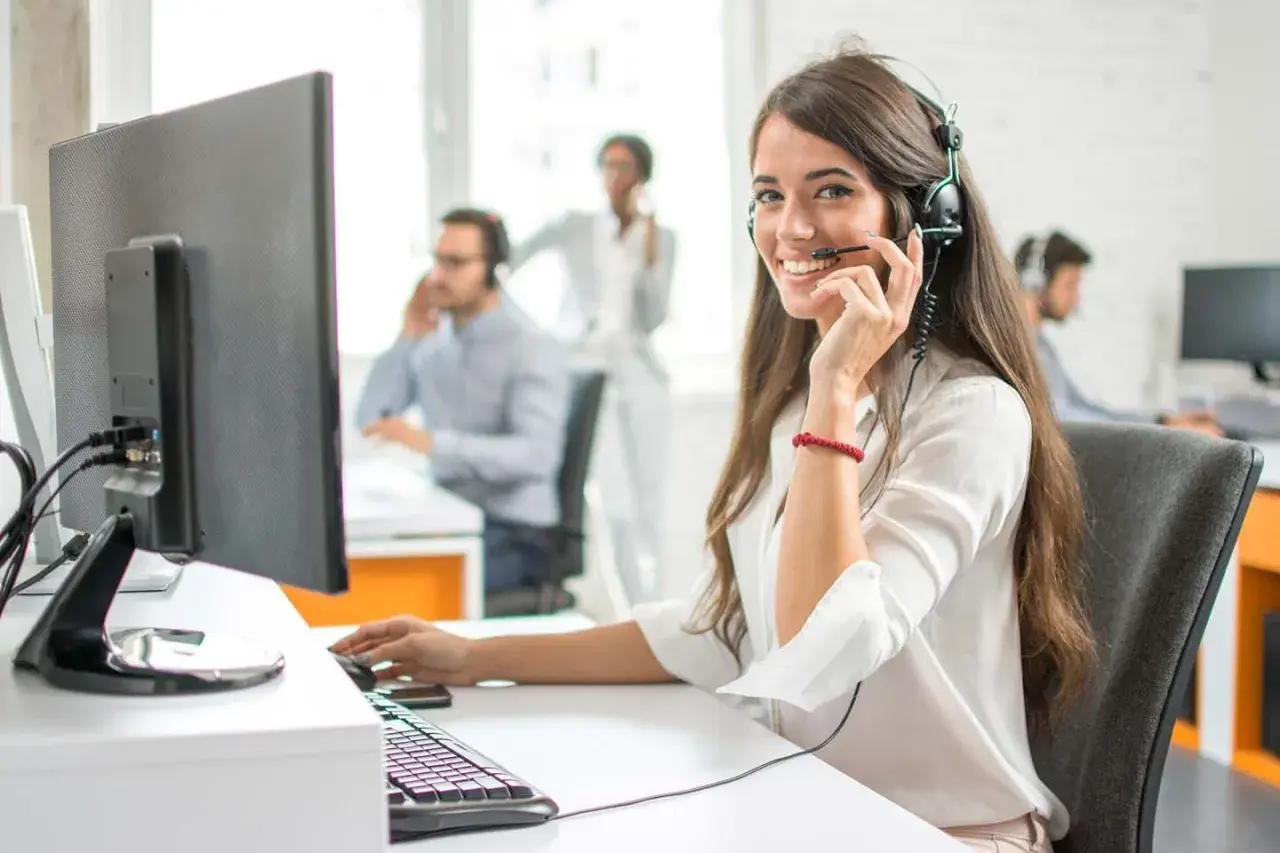 Eine freundliche Callcenter-Mitarbeiterin lächelt in die Kamera. Sie sitzt am Schreibtisch und spricht ins Headset. Sie hilft Kunden, die vielleicht auch mal Werbung widersprechen möchten.