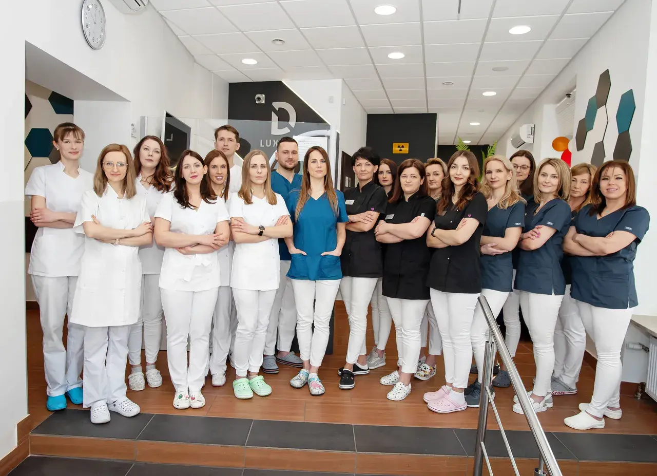 Grupa uśmiechniętych dentystów w białych i granatowych uniformach stoi w gabinecie.