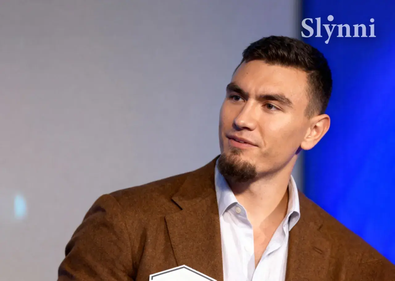 Młody mężczyzna w brązowej marynarce, z zarostem. Conan Kaźmierski wiek to temat dyskusji, ale jego pewność siebie mówi wiele.
