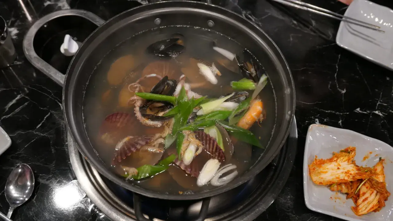 Un plat de cuisson de fruits de mer mijote dans un bouillon, avec des moules, des crevettes, des pétoncles et des poulpes.