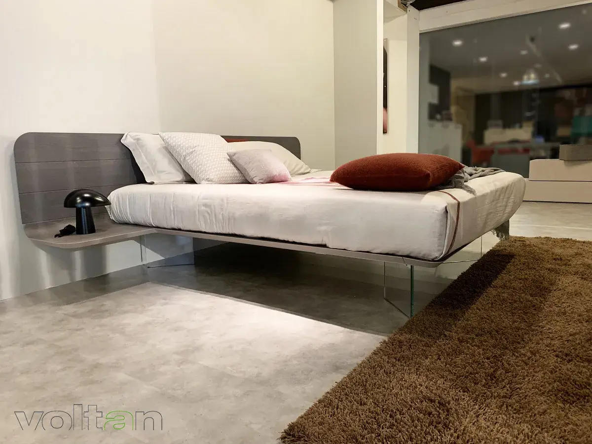 Un letto sospeso come funziona: design moderno con testiera in legno, comodino integrato e gambe in vetro trasparente.