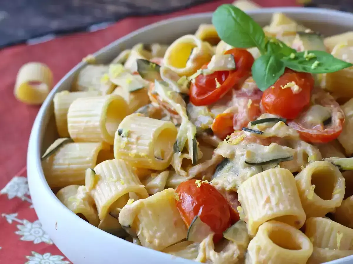 Piatto cremoso di pasta con zucchine, pomodorini e Philadelphia, guarnito con basilico fresco.