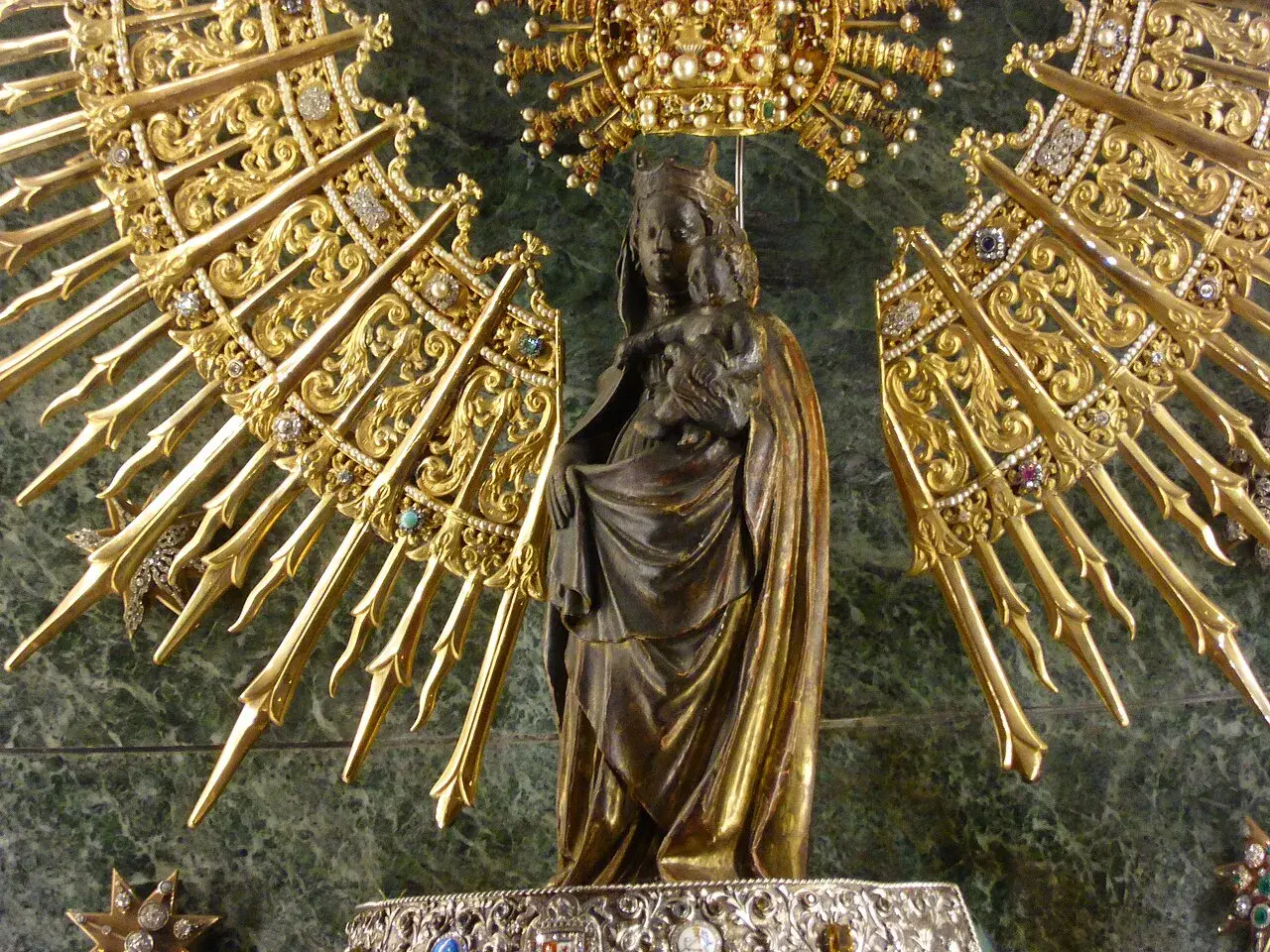 Virgen con Niño, rodeada de un resplandor dorado y joyas, evocando la solemnidad de cuando es la Pilarica.