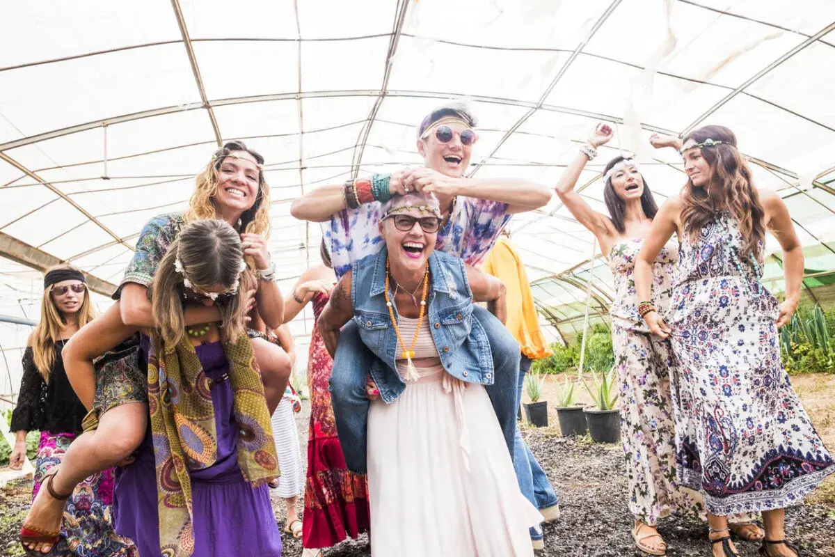 Grupa przyjaciół w stylu hippie świętuje w szklarni, śmiejąc się i bawiąc.