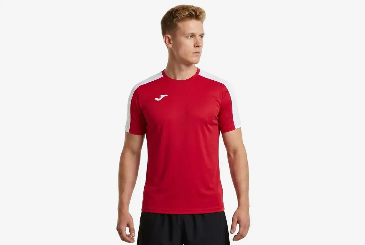 Mężczyzna w czerwonej koszulce piłkarskiej z białymi rękawami i logo Joma.