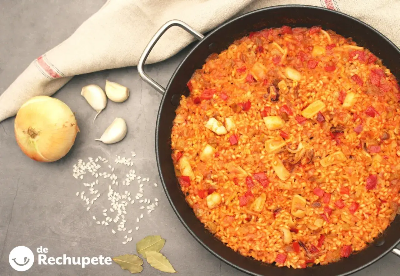 Arroz con calamares recién hecho en paellera, con ingredientes como cebolla, ajo y pimientos. ¡Un plato delicioso!