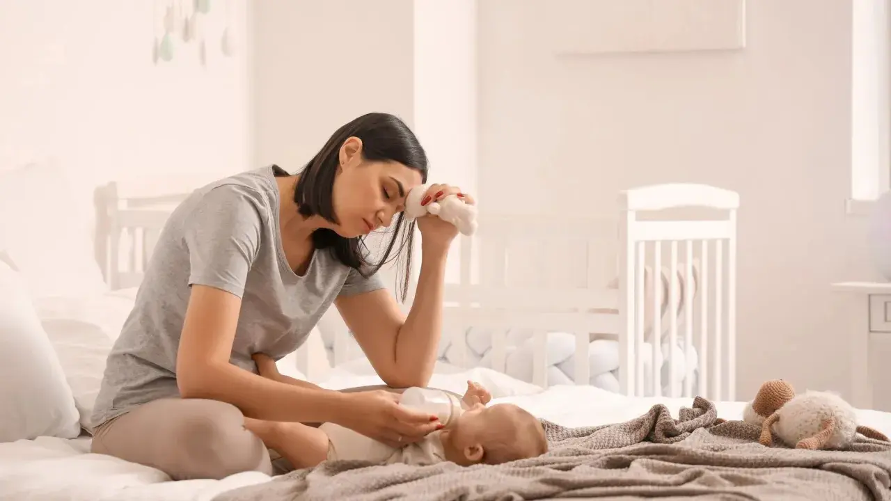 Madre esausta che allatta il neonato, con un peluche in mano, simbolo della sua lotta contro la depressione post partum.
