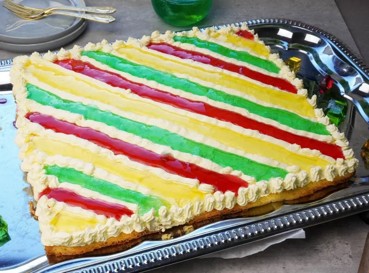 Bunte Philadelphia Torte mit Waldmeister-Aroma, dekoriert mit Sahnetuffs und roten Fruchtstreifen.