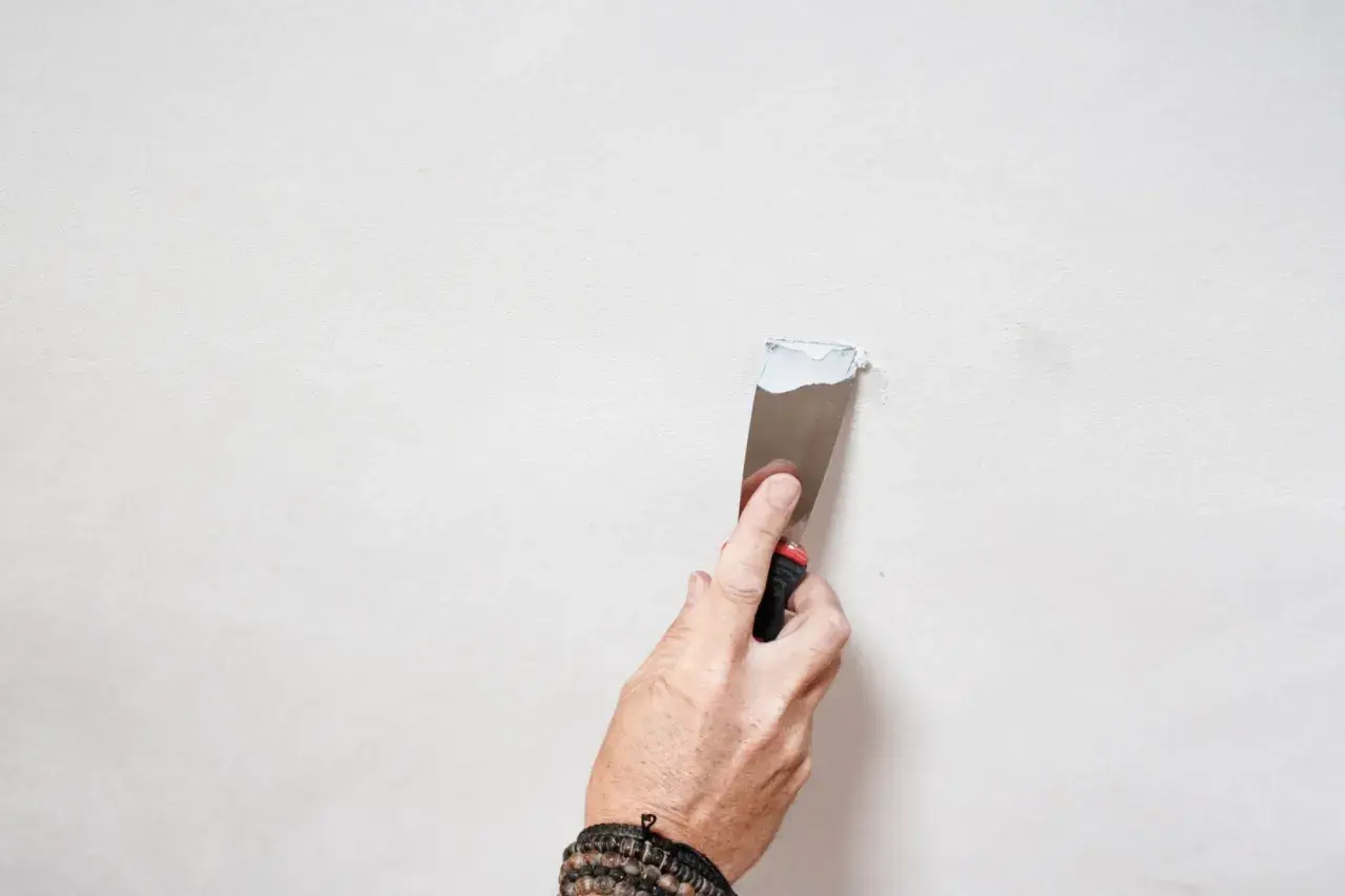 Mano con spatola applica stucco bianco su parete, un passo per come pitturare di bianco una parete gialla.