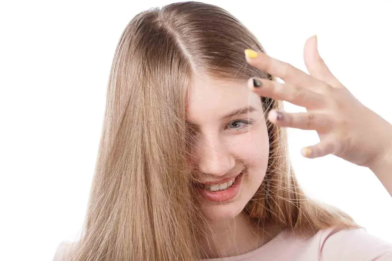 Chica sonriente con cabello rubio que se toca la frente, buscando cómo quitar la electricidad del pelo.